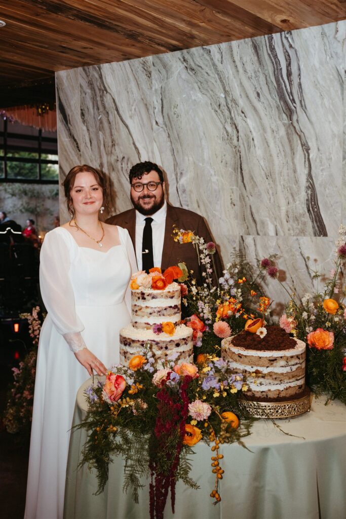 Newlyweds smile at The Sage wedding celebration in Birmingham with two wedding cakes and colorful party details