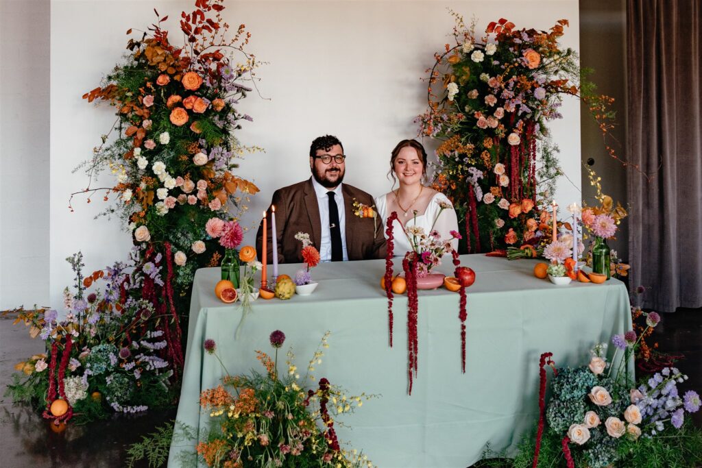 Newlyweds are seated at their sweetheart table at The Sage wedding reception in Birmingham featuring bright floral centerpieces and green table linens