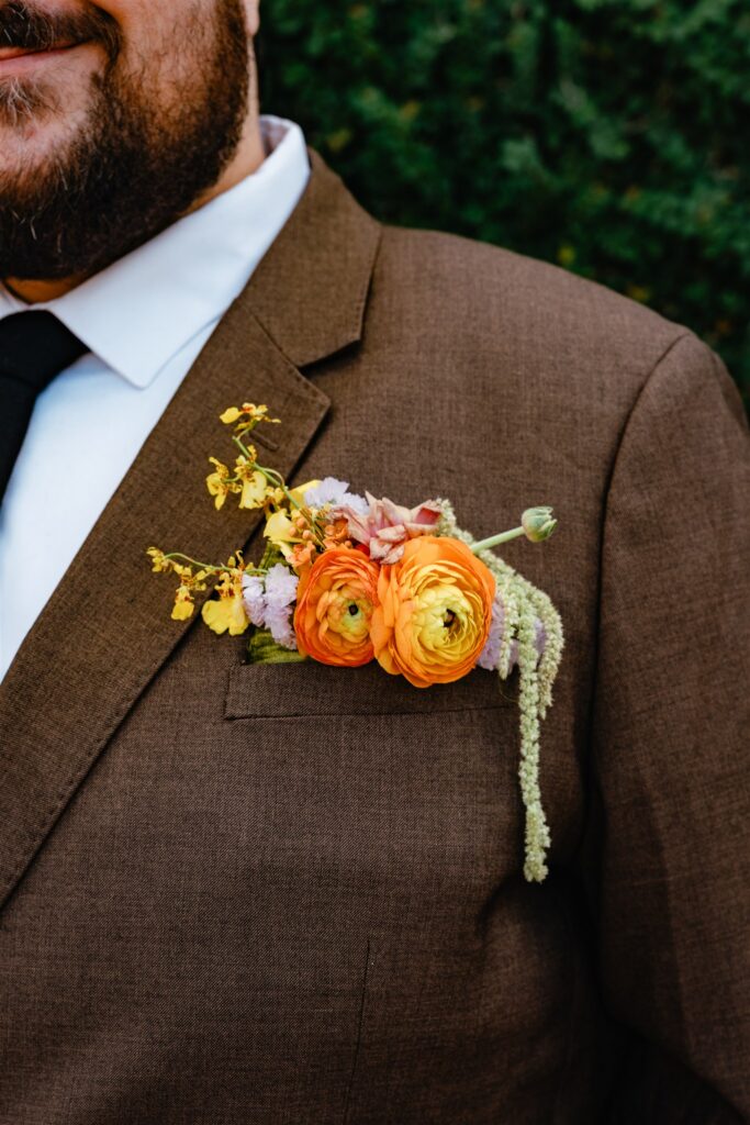 A colorful boutonniere is photographed against a brown suit in a detail shot by an Alabama wedding photographer