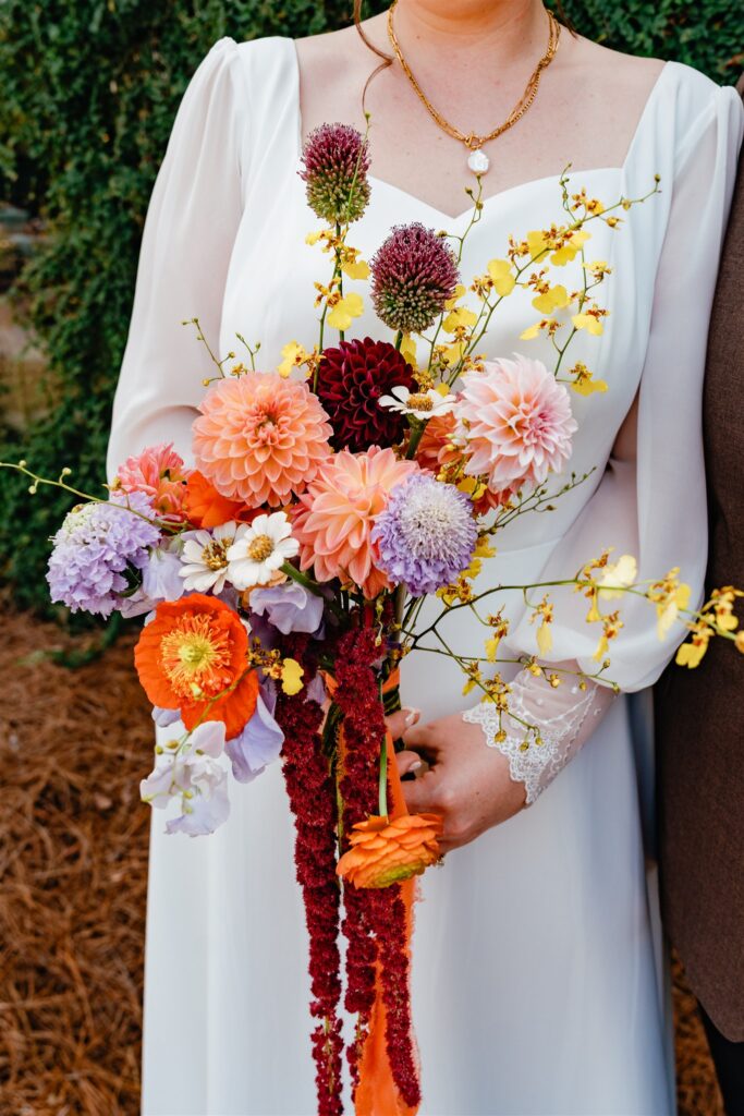 A colorful bridal bouquet featuring lavender, peach, and orange blooms is captured in a detail shot by an Alabama wedding photographer 