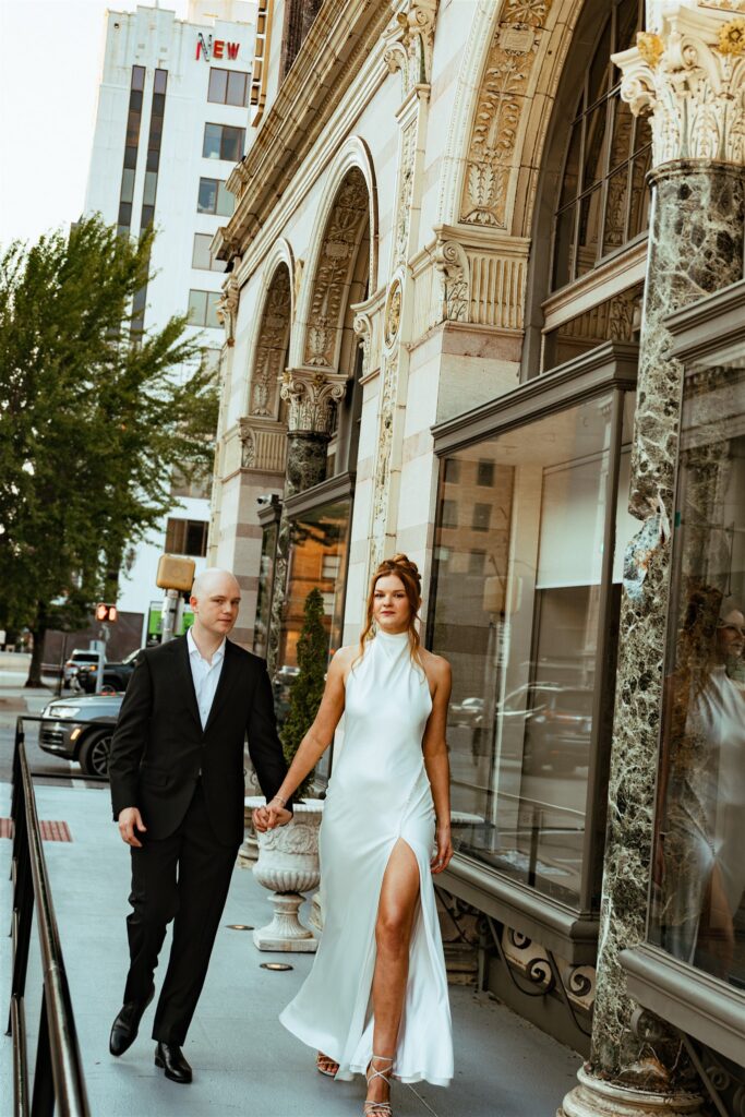 Newlyweds hold hands in their wedding attire as they stroll the sidewalks of Birmingham AL outside The Florentine 