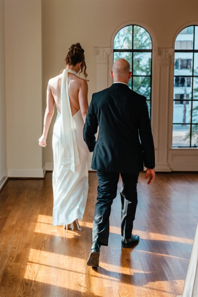 Newlyweds hold hands as they walk across the wooden floors at The Florentine in Birmingham AL