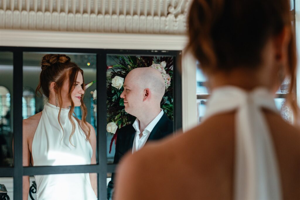 Newlyweds smile in a mirrored reflection in a photo taken at their elopement reception held at The Florentine Birmingham