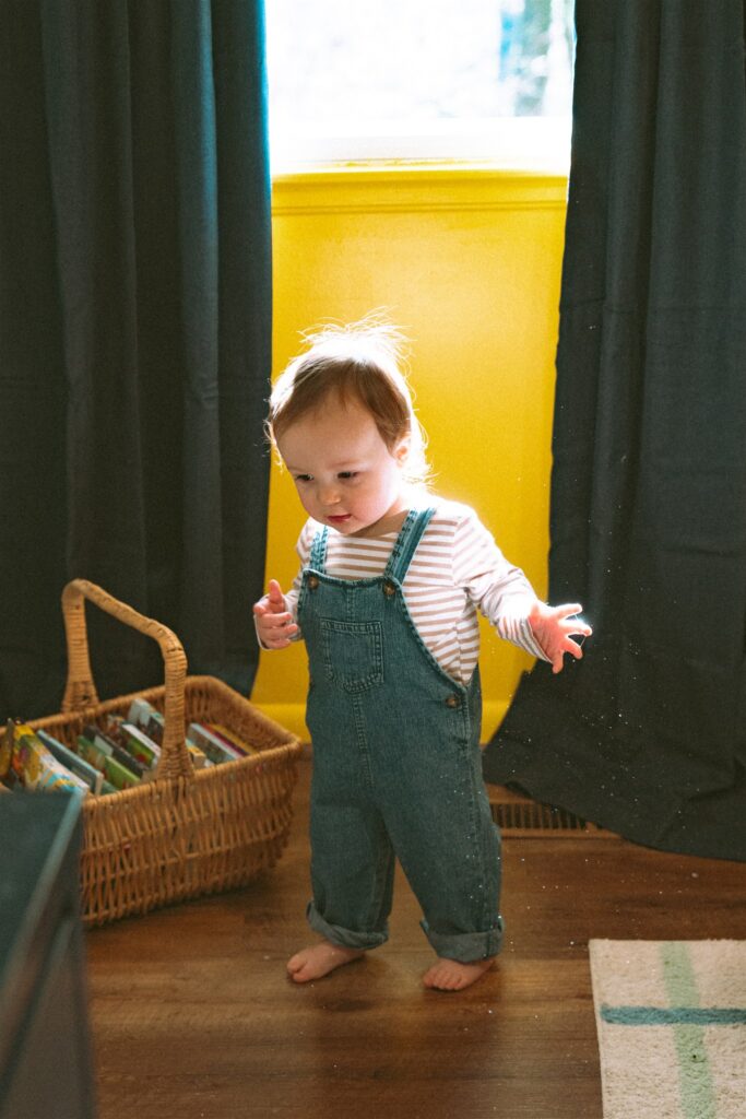 A toddler boy is pictured in his brightly colored nursery during a family photo session with a family photographer birmingham al