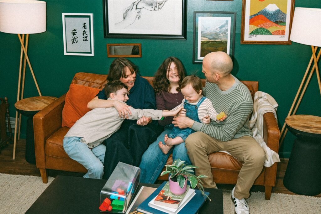 A family of five laugh together on a leather sofa during an in home photoshoot with an alabama family photographer