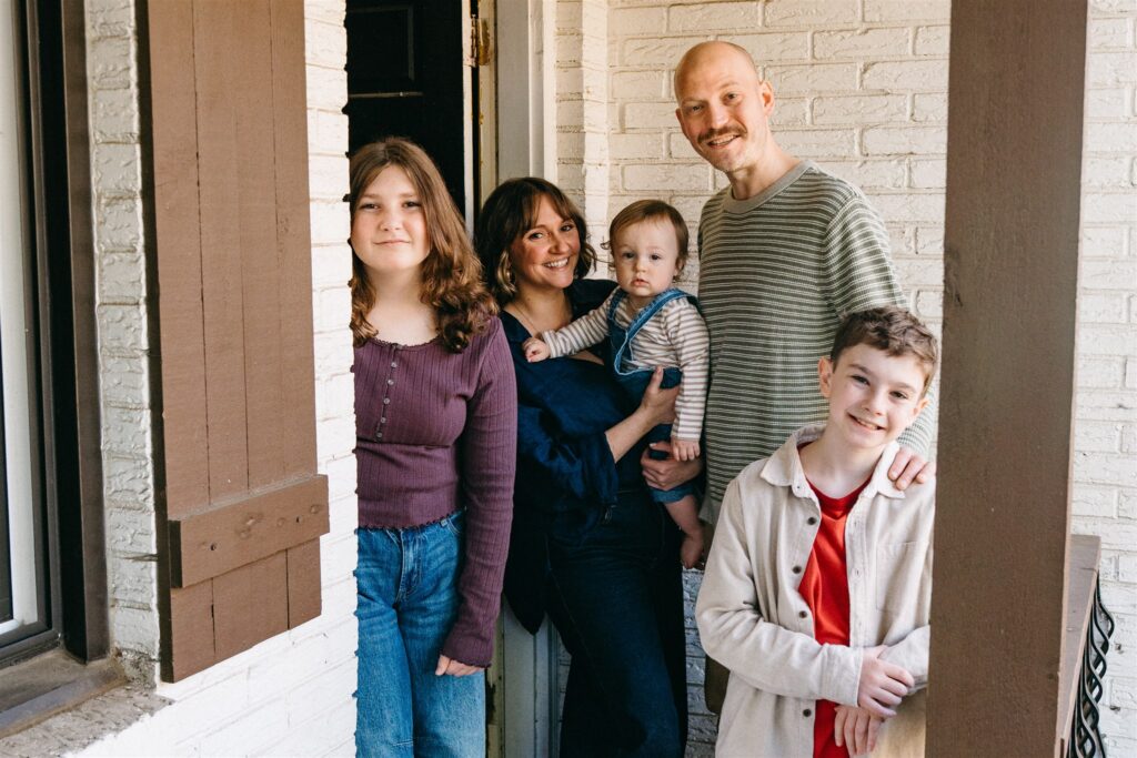 A family smiles for a photo on their front porch during an in home session with a family photographer in birmingham al