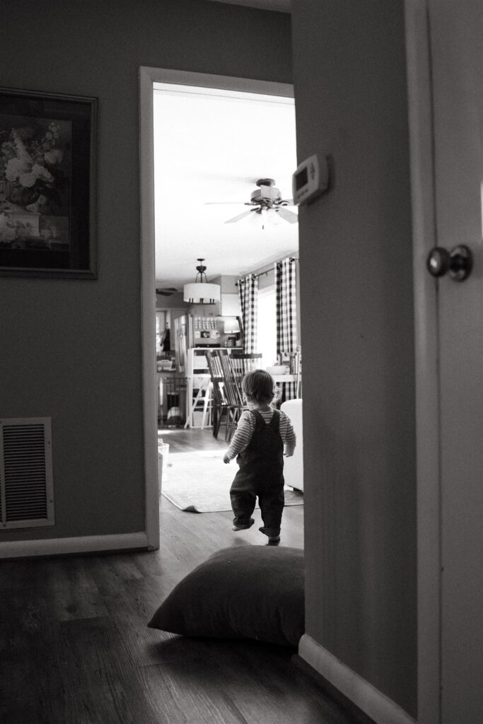 A b+w image depicts a toddler in overalls walking away from the camera during family portraits birmingham alabama 