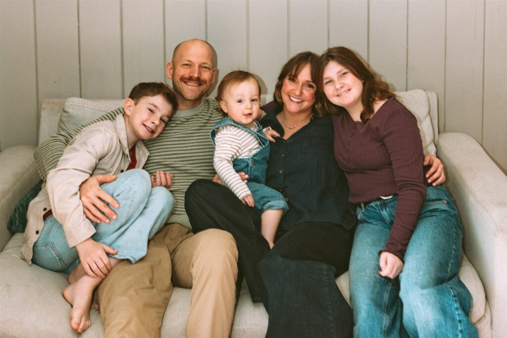 A Birmingham family of 5 smile seated on their living room furniture during an in-home session with an alabama family photographer