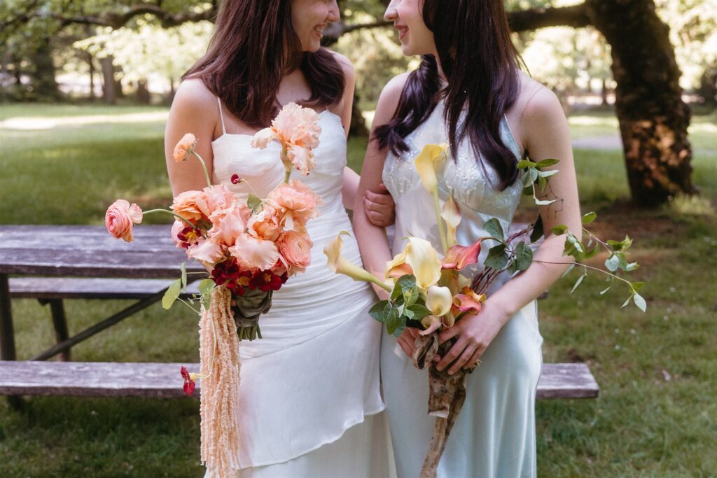 Oregon coast elopement brides standing arm in arm holding vibrant wedding bouquets