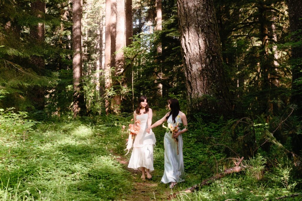 A PNW elopement photographer captures two brides walking through the forest at their Silver Falls elopement