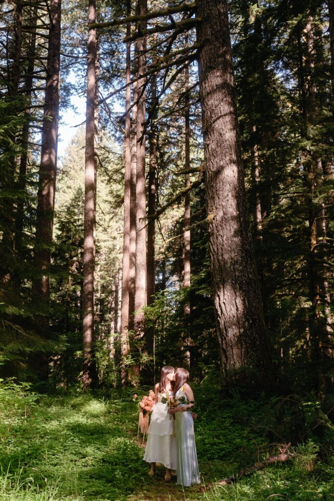Two brides share a kiss beneath the forest canopy in Silver Falls at their Portland Oregon Elopement