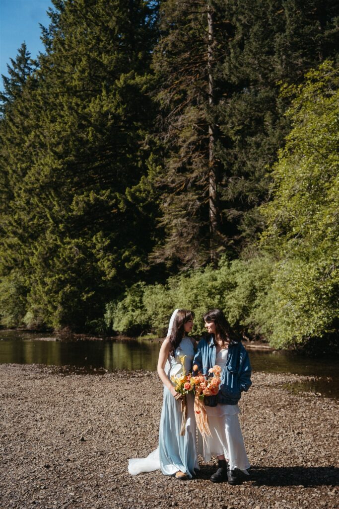 A couple stands on the banks of a river at their Portland Oregon Elopement in Silver Falls State Park
