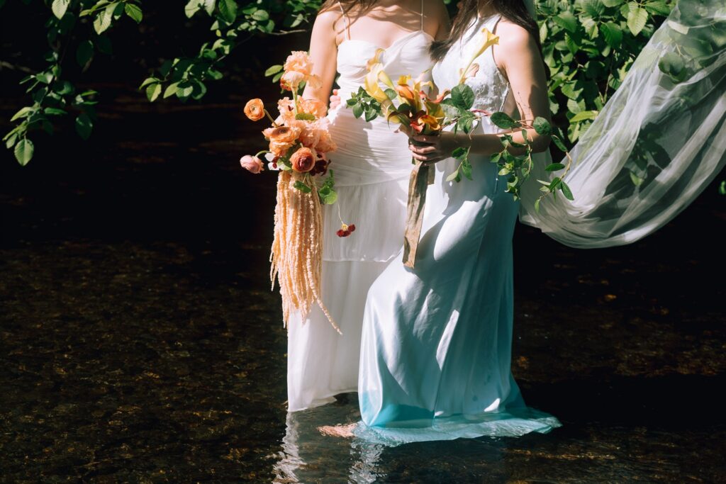 Oregon coast elopement brides standing in water holding vibrant wedding bouquets