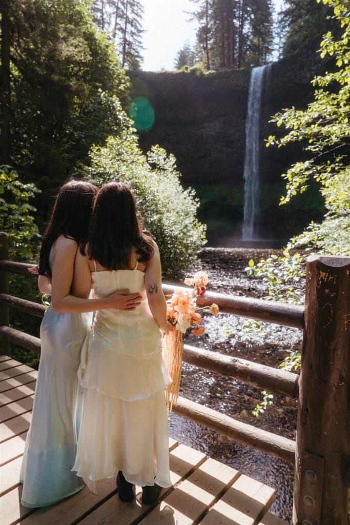 Two brides look out over the water at a waterfall during their Portland Oregon elopement
