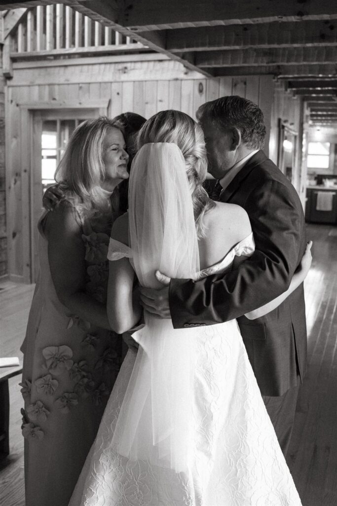 A black and white portrait taken by a Tennessee elopement photographer showcases a bride being embraced by her family before her ceremony. 