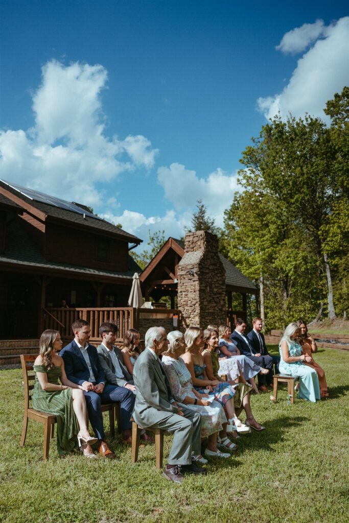 Guests are seated on the lawn of a cabin in the Smoky Mountains at a Pigeon Forge elopement ceremony. 
