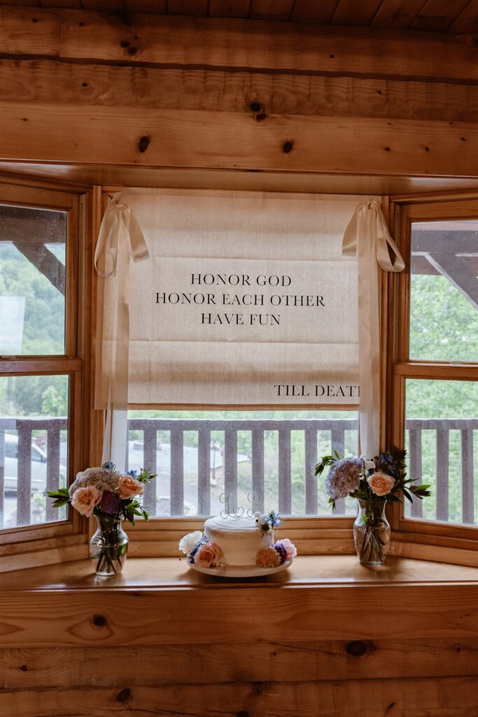 A wedding cake and florals are photographed in the window of a cabin before a Pigeon Forge elopement. 