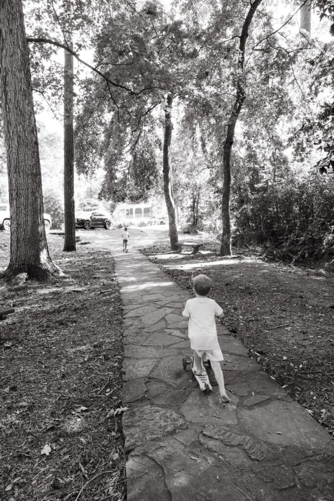 A black and white image of a little boy riding his scooter during a family photography Birmingham session at a local park.