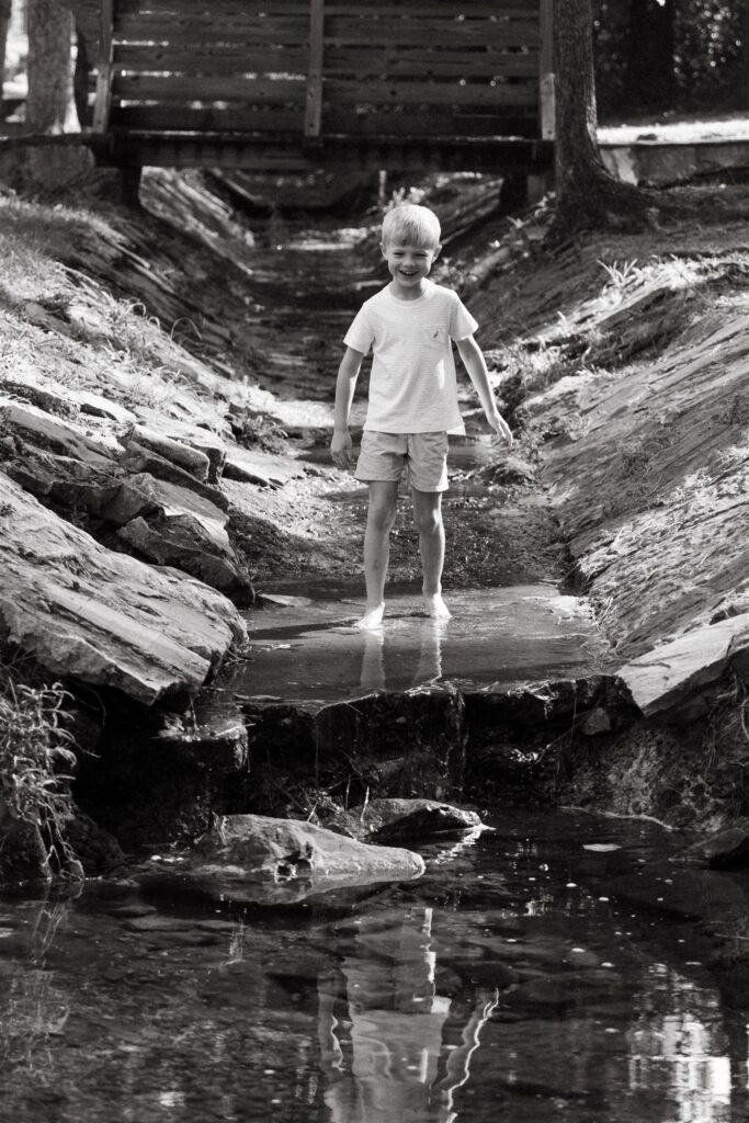 A young boy explores a creek in a black and white image taken during candid family photos Birmingham AL.