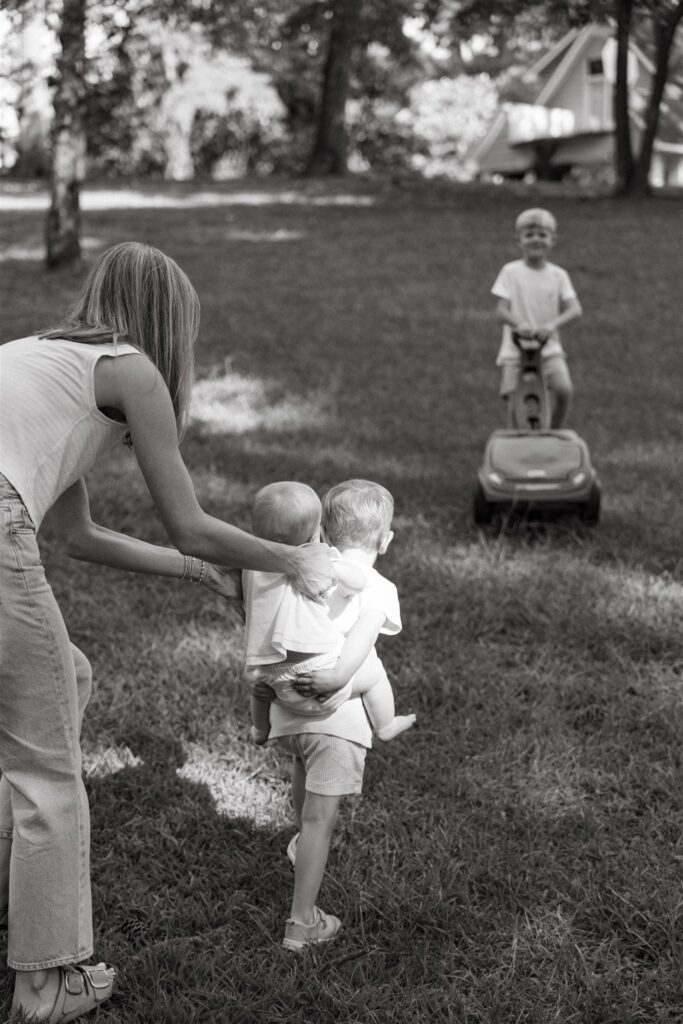 A mother supports her baby being carried by an older brother in a b+w image taken during family photography Birmingham. 