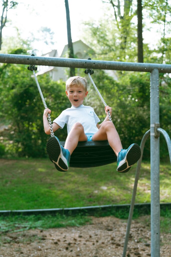 family portraits birmingham show a young boy making a silly face on a swing at a local park. 