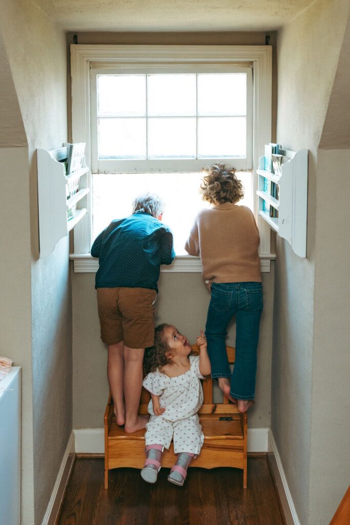 Three young children look out the window of their home during lifestyle family portraits Birmingham.