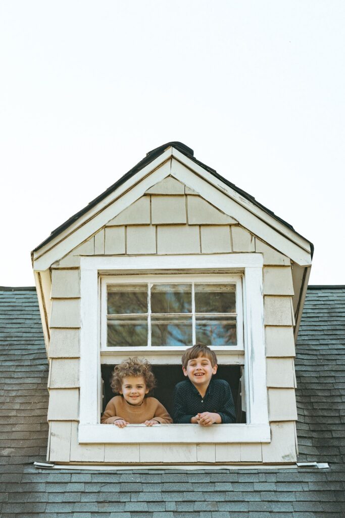 Two young brothers smile down at a  family portrait photographer in Birmingham from their bedroom window. 