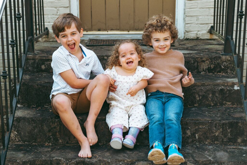 Three sibling smile together on the front stoop of their Birmingham home in a photo taken by a family portrait photographer Alabama.