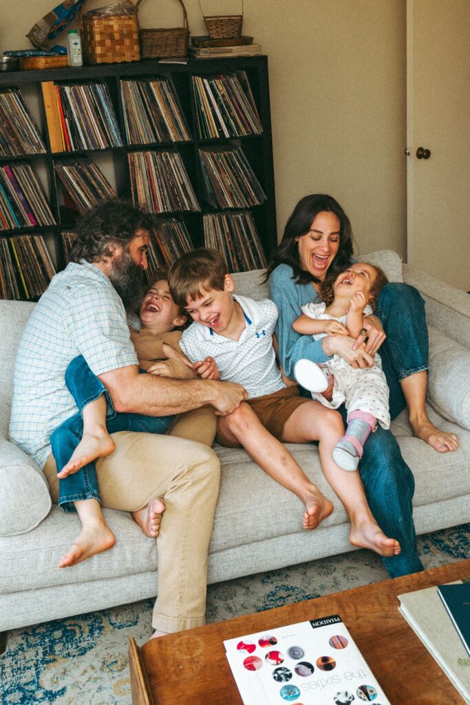 A mother & father laugh with their three children on their living room sofa during in home family portraits Birmingham. 